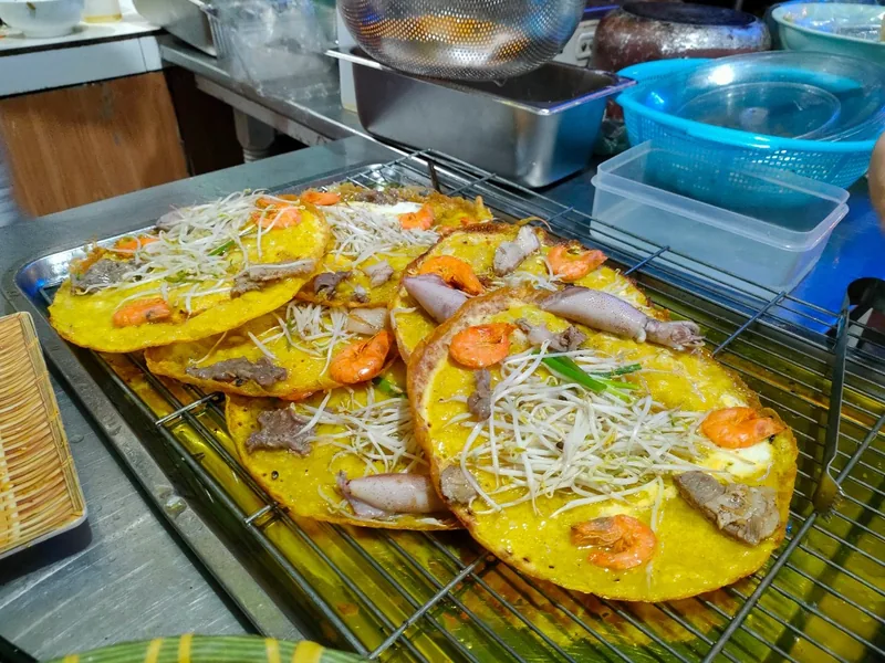 Freshly cooked Vietnamese banh xeo pancakes topped with shrimp, pork and bean sprouts cool on a wire rack in a Hoi An.
