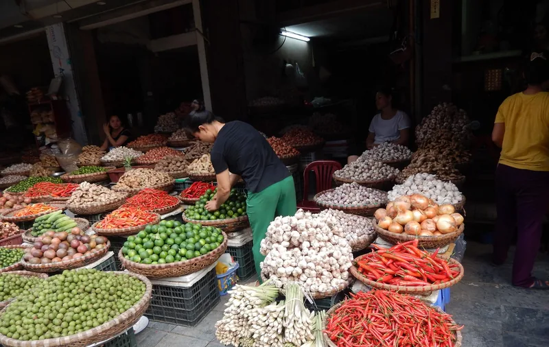 Vendor arranges baskets of chilies, garlic, onions, and limes at a market stall in Hanoi's Old Quarter.