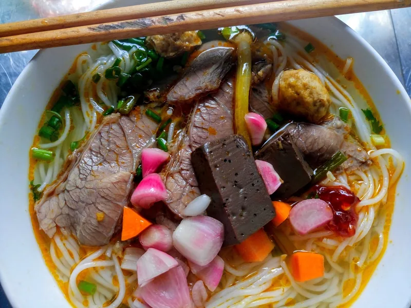 A bowl of bun bo Hue noodle soup topped with sliced beef, blood cake, and pickled vegetables in Da Nang.