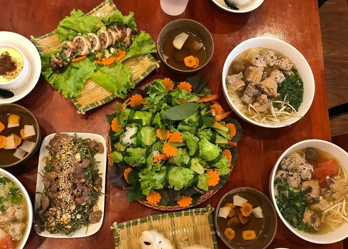 An overhead view of a Vietnamese meal with fresh salads, noodle soups, and beef dishes on a wooden table in Hanoi.