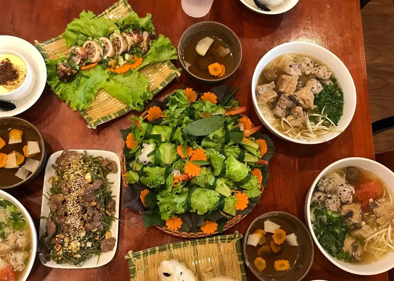 An overhead view of a Vietnamese meal with fresh salads, noodle soups, and beef dishes on a wooden table in Hanoi.