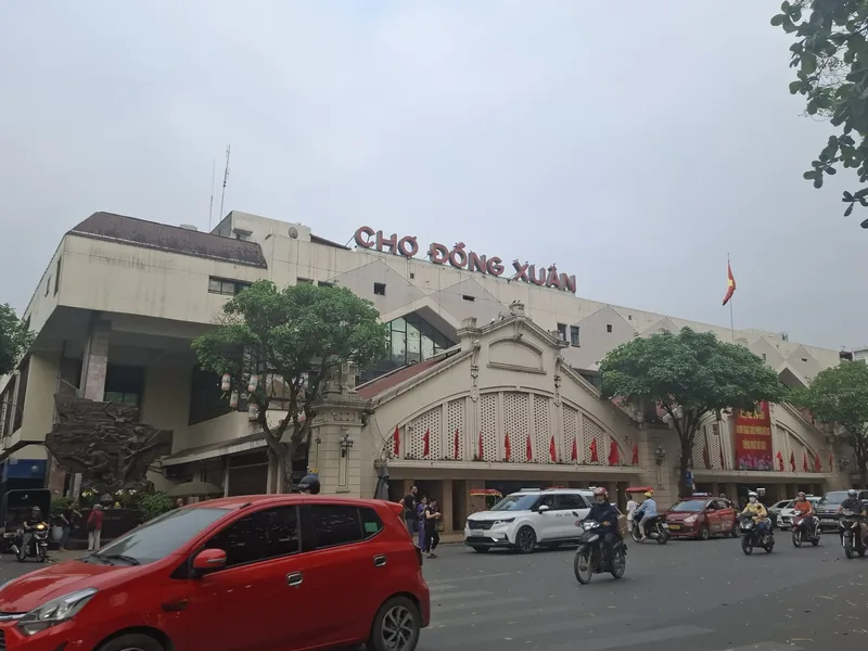 The facade of Dong Xuan Market in Hanoi with traffic passing on the busy street in front.