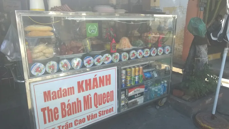A street food cart labeled Madam Khanh The Banh Mi Queen displays ingredients and drinks in Hoi An.