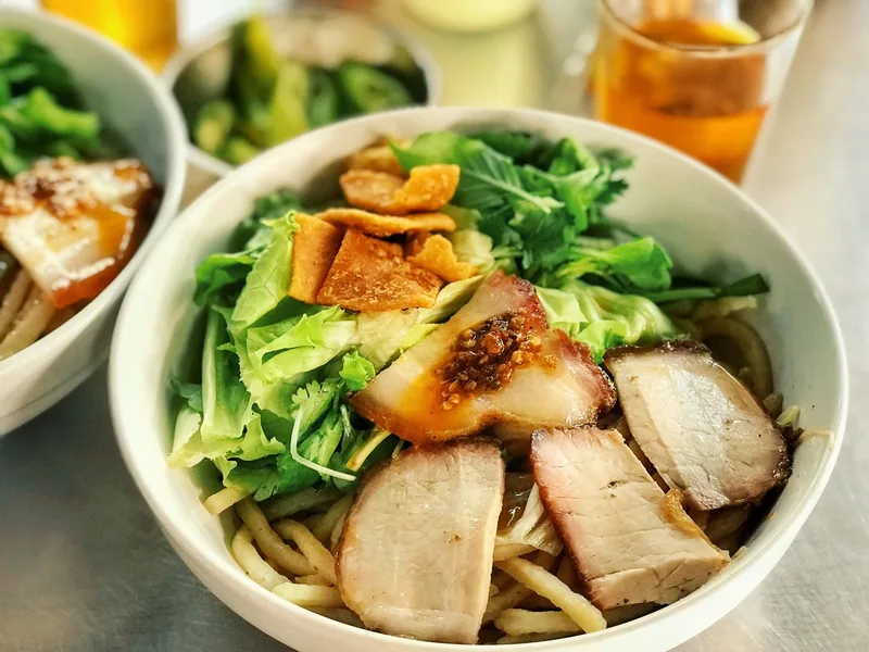 A bowl of Hoi An's cao lau noodles topped with sliced pork and fresh greens.