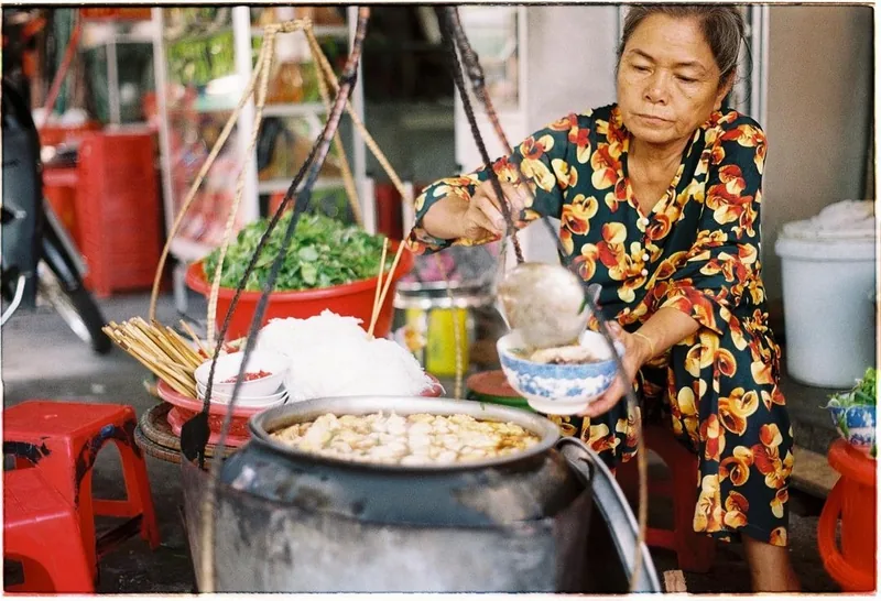 A street vendor in Hue ladles noodle soup from a large pot into a bowl at her food stall.