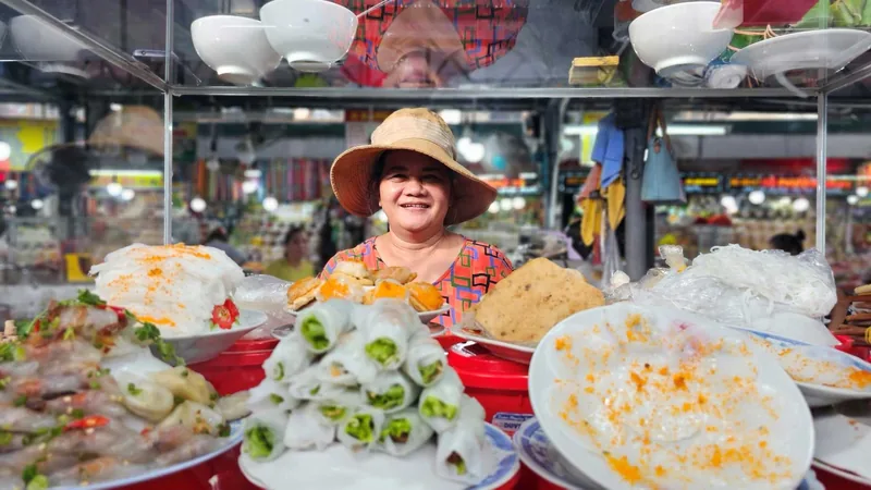 A smiling vendor in a straw hat sells fresh spring rolls and rice dishes at Dong Ba Market in Hue.