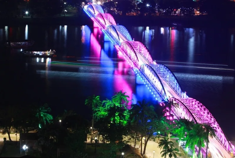 Trang Tien Bridge in Hue glows with colorful pink and blue lights over the Perfume River at night.